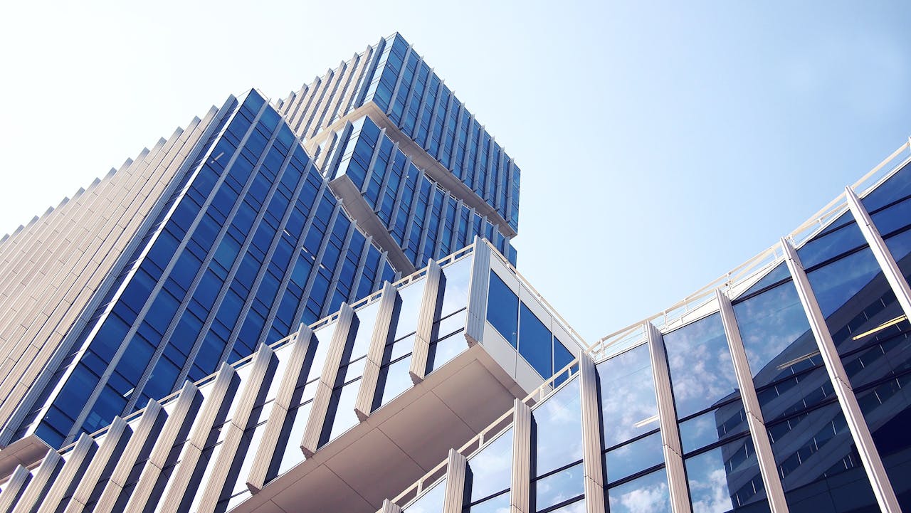 services-01 Low-angle shot of a modern skyscraper with reflective glass design under a clear blue sky.